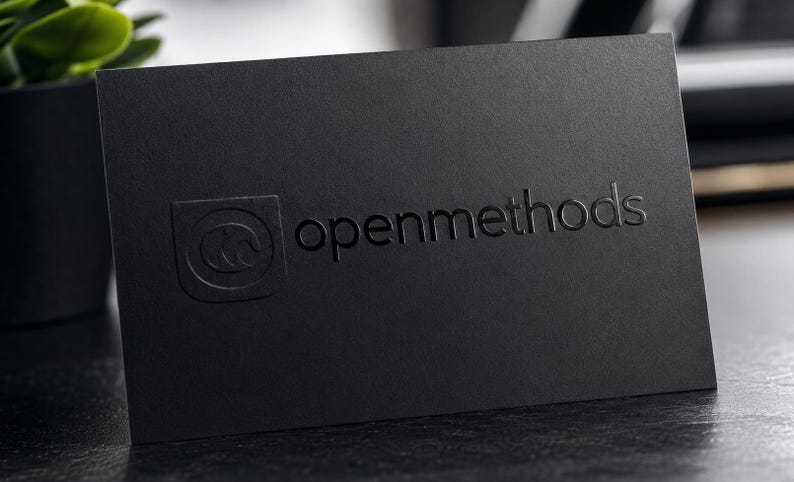 May include: A rectangular black business card featuring the text openmethods embossed on the front surface. To the left of the text is a square logo containing a stylized letter M. The card has a matte finish and a clean, professional appearance.