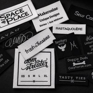 May include: A collection of rectangular fabric clothing labels in black and white. The labels feature various brand names and logos, including Space and Place, Makersnine, Sew Cozy, Rayan, trash to treasure, Territory Built Co., Hinara, MaddyMoo, dom streater, Doggie Duds, and Tasty Ties.