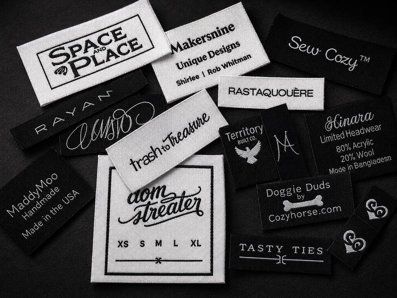 May include: A collection of rectangular fabric clothing labels in black and white. The labels feature various brand names and logos, including Space and Place, Makersnine, Sew Cozy, Rayan, trash to treasure, Territory Built Co., Hinara, MaddyMoo, dom streater, Doggie Duds, and Tasty Ties.