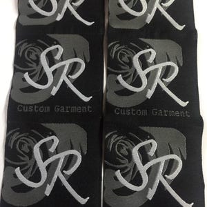 May include: Six black fabric labels arranged in two columns. Each label features a dark gray rose graphic, the light gray embroidered letters SR, and the text Custom Garment printed in a small, simple font at the bottom of each individual label.