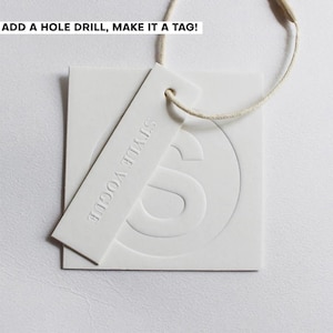 May include: A white square tag and a rectangular white tag with the text STYLE VOGUE embossed on it. Both tags are made of thick paper and are connected by a thin beige string. The text ADD A HOLE DRILL, MAKE IT A TAG! is visible at the top.