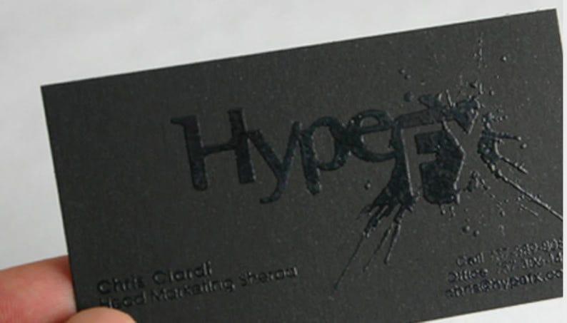 May include: A rectangular black business card featuring the embossed text HypeFX with a glossy ink splatter effect. The card includes the name Chris Ciardi, the title Head Marketing, and contact information printed in a subtle black font.