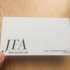 May include: White business card with the logo "JFA" in dark gray, with the website address www.jfasound.com below. The card also includes an email address and phone number. The top of the card has a textured, curved design.