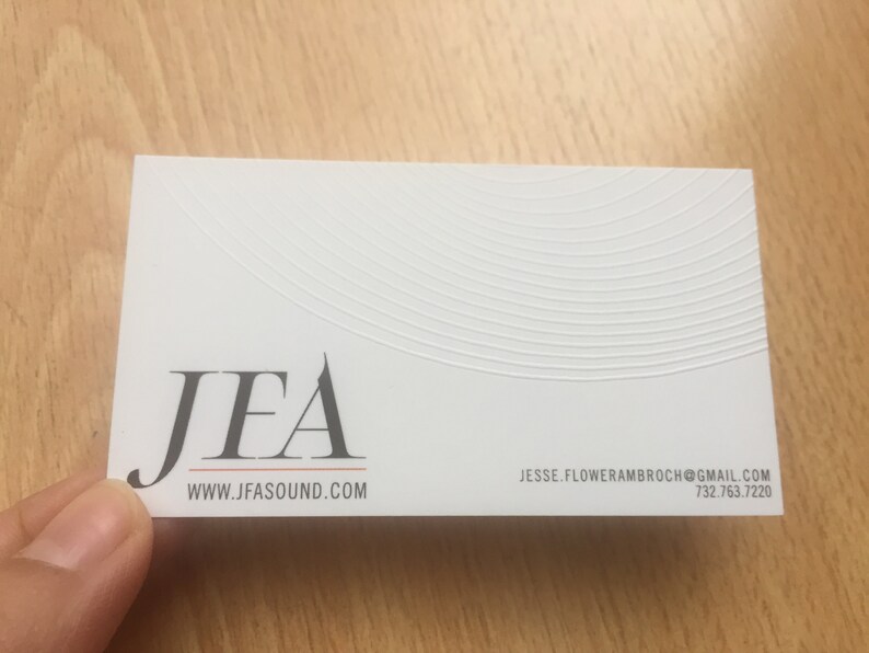 May include: White business card with the logo "JFA" in dark gray, with the website address www.jfasound.com below. The card also includes an email address and phone number. The top of the card has a textured, curved design.