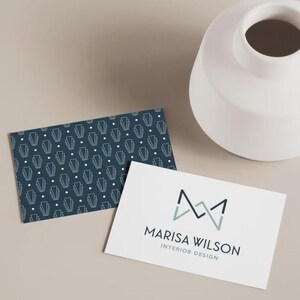May include: Two rectangular business cards. One card features a dark blue background with a repeating white geometric pattern of lines and dots. The other card is white with a dark blue and light blue logo and the text MARISA WILSON INTERIOR DESIGN.