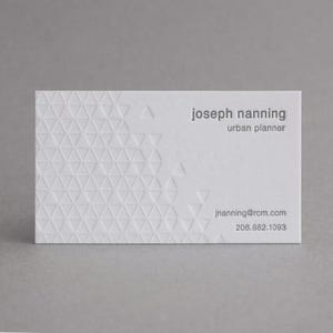 May include: A white rectangular business card featuring a debossed geometric triangle pattern on the left side. The text reads joseph nanning, urban planner, jnanning@rcm.com, and 206.882.1093 in a clean, dark gray sans-serif typeface.