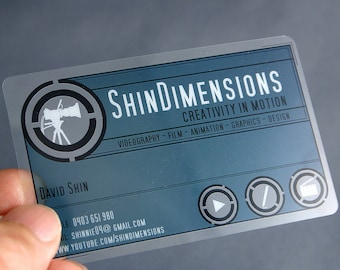 May include: A rectangular, semi-transparent business card with a blue background. It features the text ShinDimensions, Creativity in Motion, and lists services like videography, film, animation, graphics, and design, along with contact details.
