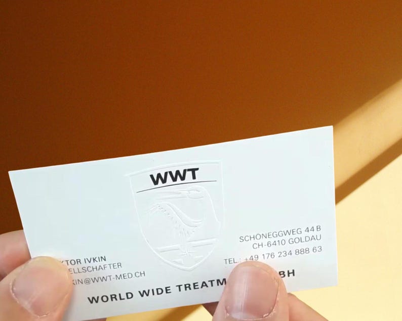 May include: A white rectangular business card featuring the black text WWT above a subtle embossed shield logo. The card includes the address Schoneggweg 44 B, CH-6410 Goldau, the phone number +49 176 234 888 63, and the text World Wide Treatment.