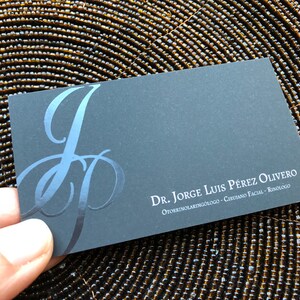 K&ouml;nnte beinhalten: Schwarze Visitenkarte mit einem silbernen J.P.-Monogramm und dem Text "Dr. Jorge Luis P&eacute;rez Olivero HNO-Arzt - Gesichtschirurg - Rhinologe"