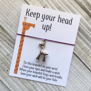 May include: A purple string bracelet with a silver giraffe charm. The card attached to the bracelet reads "Keep your head up!" and includes instructions for making a wish.