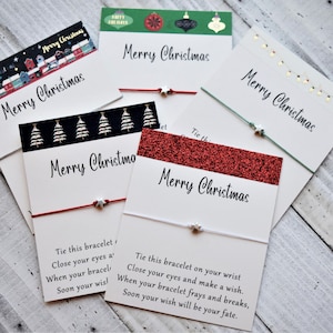 May include: Five Christmas themed friendship bracelets with silver star charms. Each bracelet is tied to a card with the text "Merry Christmas" and instructions on how to make a wish.