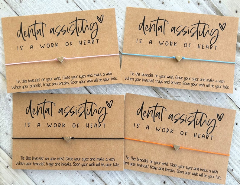 Peut inclure: Quatre cartes brunes avec le texte "dental assisting is a work of heart" et un petit charme de c&oelig;ur en or attach&eacute; &agrave; un bracelet en ficelle. Chaque carte a un bracelet en ficelle de couleur diff&eacute;rente&nbsp;: rose, bleu, noir et orange.
