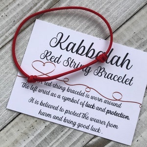 Puede incluir: Pulsera de cuerda roja con una tarjeta que dice "Kabbalah Red String Bracelet" y explica que la pulsera se lleva alrededor de la mu&ntilde;eca izquierda como s&iacute;mbolo de suerte y protecci&oacute;n. Se cree que protege al usuario del da&ntilde;o y trae buena suerte.