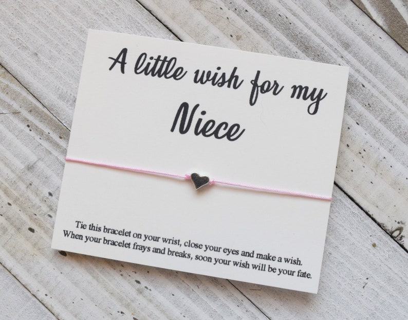 May include: A white card with the text "A little wish for my Niece" and a pink string bracelet with a small silver heart charm. The card includes instructions for making a wish.