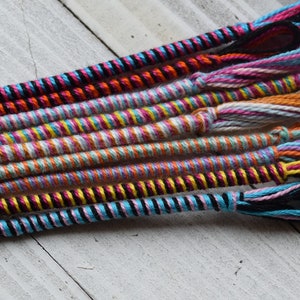 May include: A collection of colorful braided cords with tassels. The cords are made of different colors of yarn, including pink, blue, yellow, orange, and black.