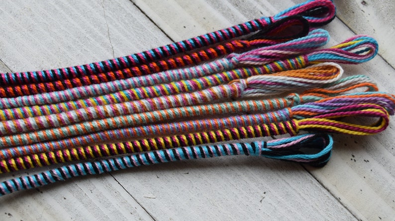 May include: A collection of colorful braided cords with tassels. The cords are made of different colors of yarn, including pink, blue, yellow, orange, and black.