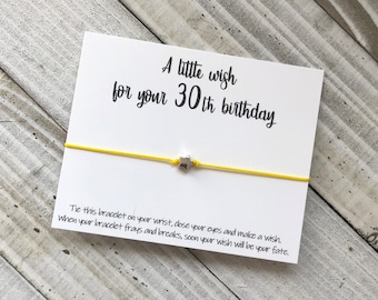 May include: A white card with the text "A little wish for your 30th birthday" and a yellow string bracelet with a silver star charm. The card instructs the recipient to tie the bracelet on their wrist, close their eyes, make a wish, and when the bracelet frays, their wish will come true.