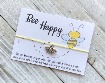 May include: A yellow string bracelet with a silver bee charm. The card attached to the bracelet reads "Bee Happy" and includes instructions to tie the bracelet on your wrist, close your eyes, make a wish, and when the bracelet frays and breaks, your wish will come true.