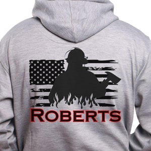 May include: A gray hooded sweatshirt with a black and white American flag design featuring a firefighter silhouette holding an axe. The text "ROBERTS" is printed below the flag.
