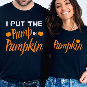 May include: Two black t-shirts with a pumpkin design. The first shirt says "I put the pump in pumpkin" with a small pumpkin graphic on each side of the text. The second shirt says "Pumpkin" with a small pumpkin graphic on the right side of the text.