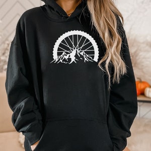 May include: Black hoodie with a white graphic of a mountain range with a bicycle wheel in the background.