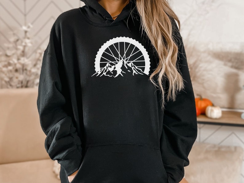 May include: Black hoodie with a white graphic of a mountain range with a bicycle wheel in the background.