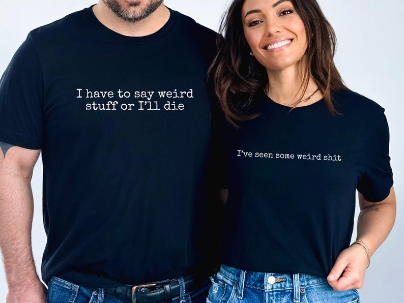May include: Two black t-shirts with white text. One shirt reads "I have to say weird stuff or I'll die," and the other says "I've seen some weird shit." Both shirts are paired with blue jeans.