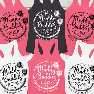 May include: A collection of racerback tank tops in various colors, including pink, black, and white. Each tank top features a circular design with the words "Muddy Buddies 2026" and "Muddy Girl Mud Run."