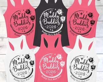 May include: A collection of racerback tank tops in various colors, including pink, black, and white. Each tank top features a circular design with the words "Muddy Buddies 2026" and "Muddy Girl Mud Run."
