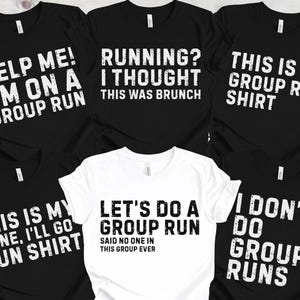May include: A collection of black and white graphic t-shirts with humorous running-themed slogans. The shirts feature phrases like "Help Me! I'm on a Group Run" and "Let's Do a Group Run".