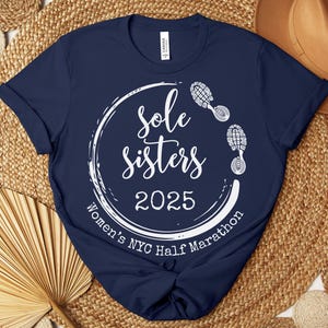 May include: Navy blue t-shirt with a white circle graphic that says "Sole Sisters 2025 Women's NYC Half Marathon" with white footprints around the circle.