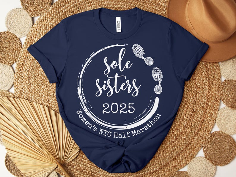 May include: Navy blue t-shirt with a white circle graphic that says "Sole Sisters 2025 Women's NYC Half Marathon" with white footprints around the circle.