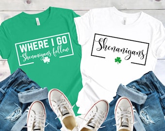 Puede incluir: Dos camisetas, una verde y una blanca, con temática del Día de San Patricio. La camiseta verde dice "Where I Go Shenanigans Follow" con un trébol. La camiseta blanca dice "Shenanigans" con un trébol.