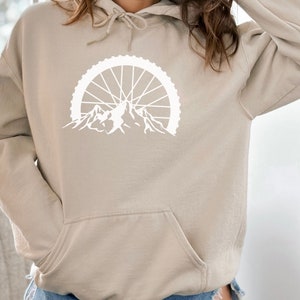 May include: A beige hoodie with a white graphic of a mountain range with a bicycle wheel above it.