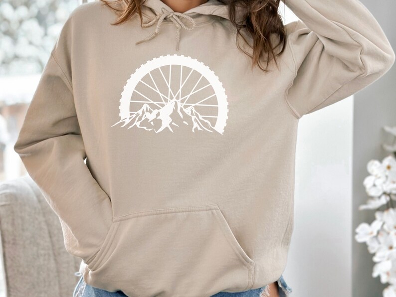 May include: A beige hoodie with a white graphic of a mountain range with a bicycle wheel above it.