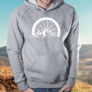 May include: A gray hooded sweatshirt with a white graphic of a mountain range with a bicycle wheel behind it.