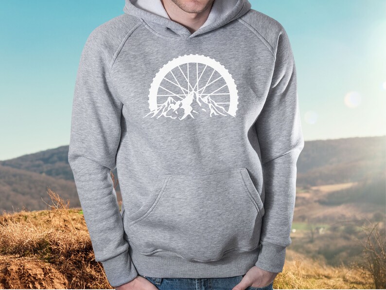 May include: A gray hooded sweatshirt with a white graphic of a mountain range with a bicycle wheel behind it.
