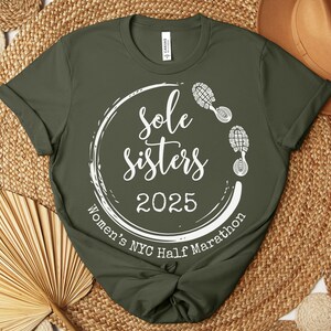 May include: A green t-shirt with a white circle design that says "Sole Sisters 2025 Women's NYC Half Marathon" with a footprint graphic.