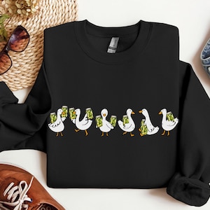 May include: Black crewneck sweatshirt featuring a line of cartoon ducks, each holding a green beer stein. The ducks are white with yellow beaks and feet. The design is centered on the front of the sweatshirt.