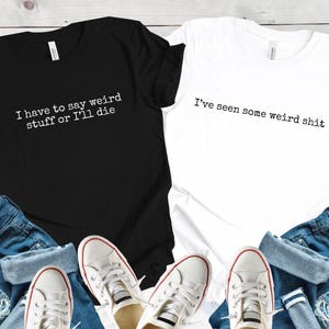 May include: Black and white t-shirts with humorous text. The black shirt reads "I have to say weird stuff or I'll die," and the white shirt says "I've seen some weird shit." The shirts are paired with blue jeans and white sneakers.