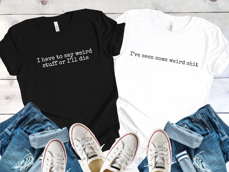 May include: Black and white t-shirts with humorous text. The black shirt reads "I have to say weird stuff or I'll die," and the white shirt says "I've seen some weird shit." The shirts are paired with blue jeans and white sneakers.