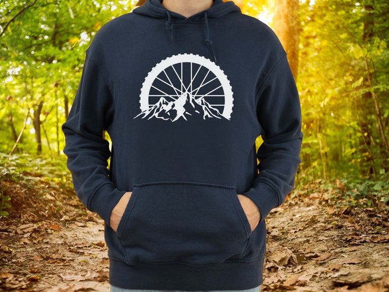 May include: A navy blue hoodie with a white graphic of a mountain range with a bicycle wheel in the background.