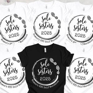 May include: Five white t-shirts with black text and graphics. The text reads "Sole Sisters 2025 Women's NYC Half Marathon". The graphic is a circle with footprints around it.
