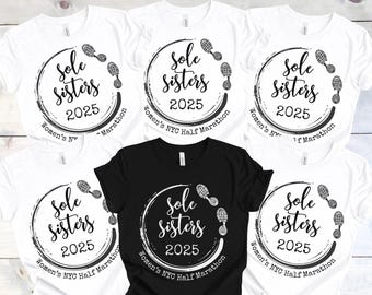 May include: Five white t-shirts with black text and graphics. The text reads "Sole Sisters 2025 Women's NYC Half Marathon". The graphic is a circle with footprints around it.