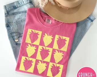May include: Pink t-shirt with a yellow and pink strawberry print. The strawberries are arranged in a checkered pattern.