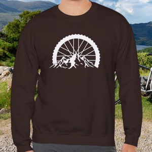 May include: A brown long-sleeve sweatshirt with a white graphic of a mountain range with a bicycle wheel in the background.