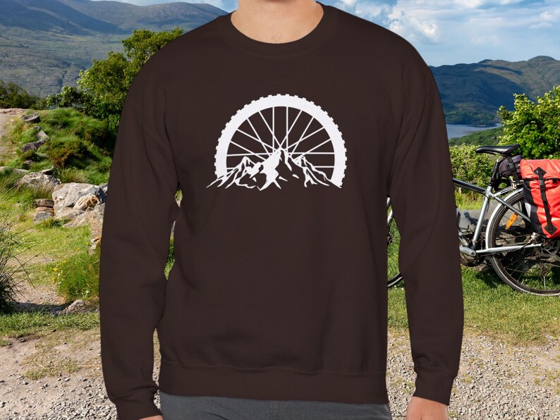 May include: A brown long-sleeve sweatshirt with a white graphic of a mountain range with a bicycle wheel in the background.
