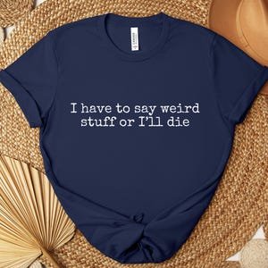 May include: Navy blue t-shirt with the text "I have to say weird stuff or I'll die" in white. The shirt is made of a soft material and has short sleeves. The shirt is knotted at the bottom.