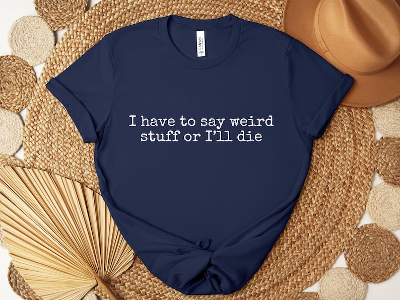 May include: Navy blue t-shirt with the text "I have to say weird stuff or I'll die" in white. The shirt is made of a soft material and has short sleeves. The shirt is knotted at the bottom.