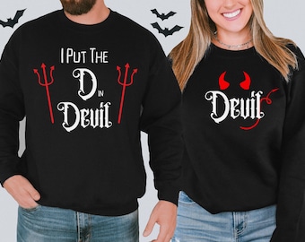 May include: Two black sweatshirts with a Halloween theme. One sweatshirt says "I put the D in Devil" with red devil horns and a red trident. The other sweatshirt says "Devil" with red devil horns.